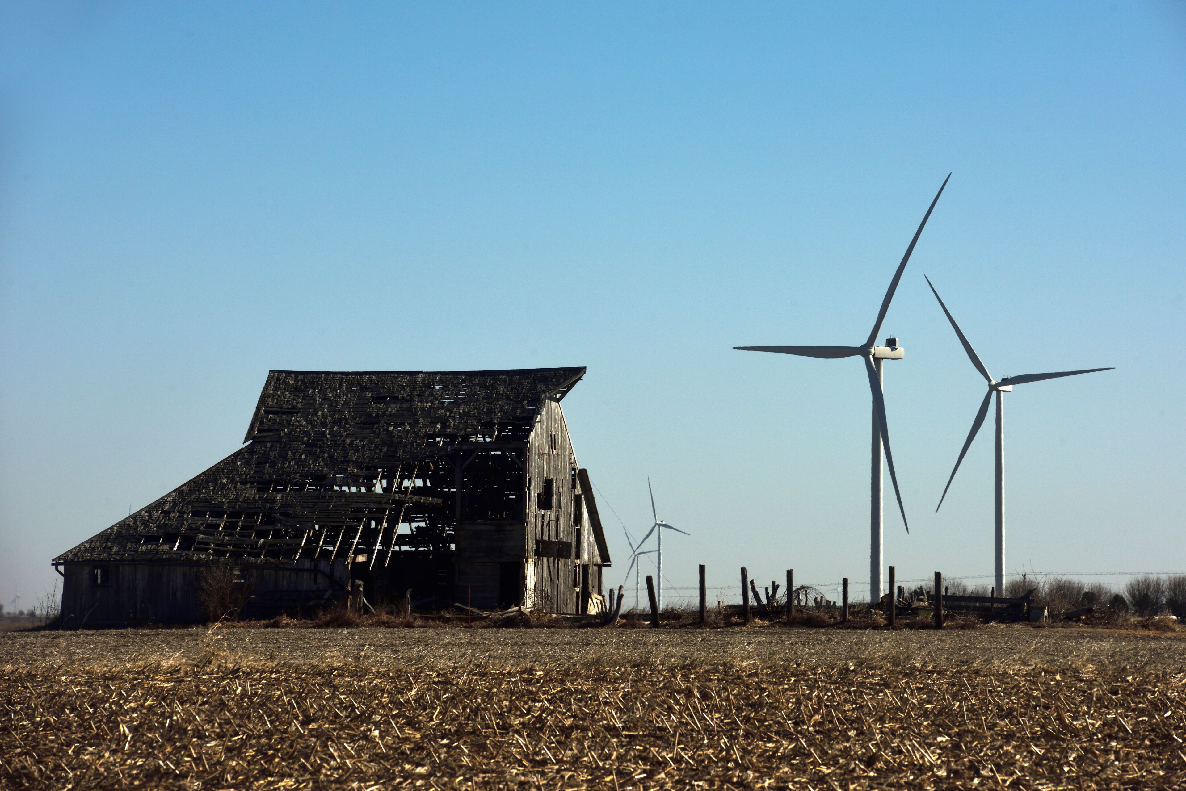 A dilapidated barn, wind turbines, and a field of harvested crops.