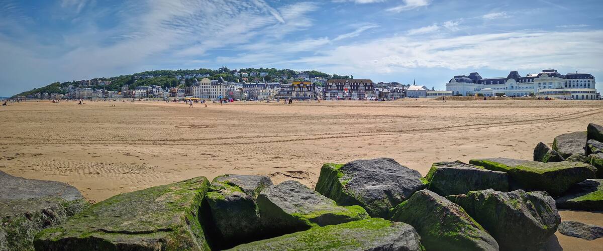 A beach with large rocks in the foreground, a sandy shore, and a town with historic buildings in the background.