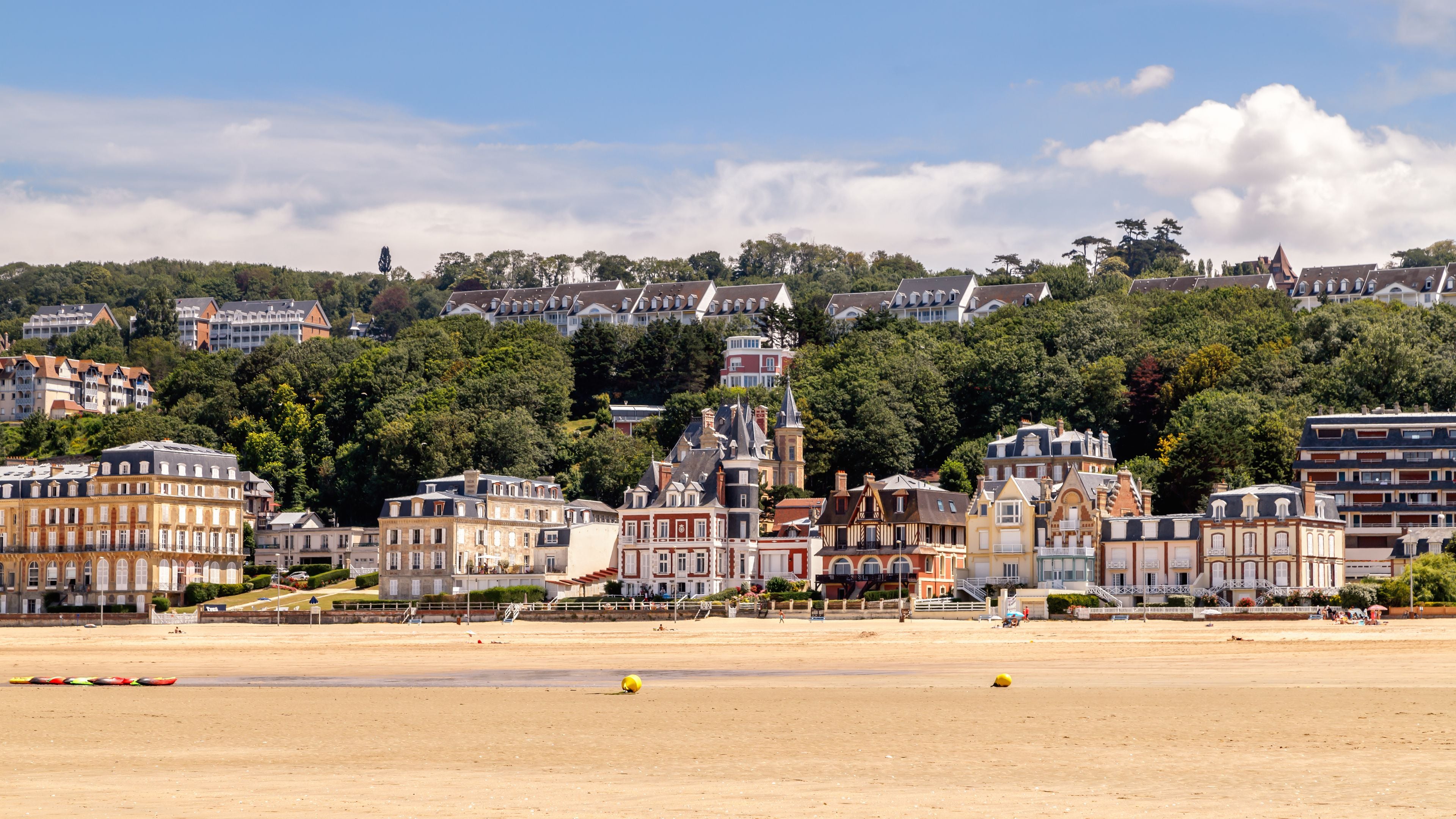 Une ville côtière dotée de bâtiments historiques, d’une plage de sable et, en arrière-plan, d’une colline boisée.