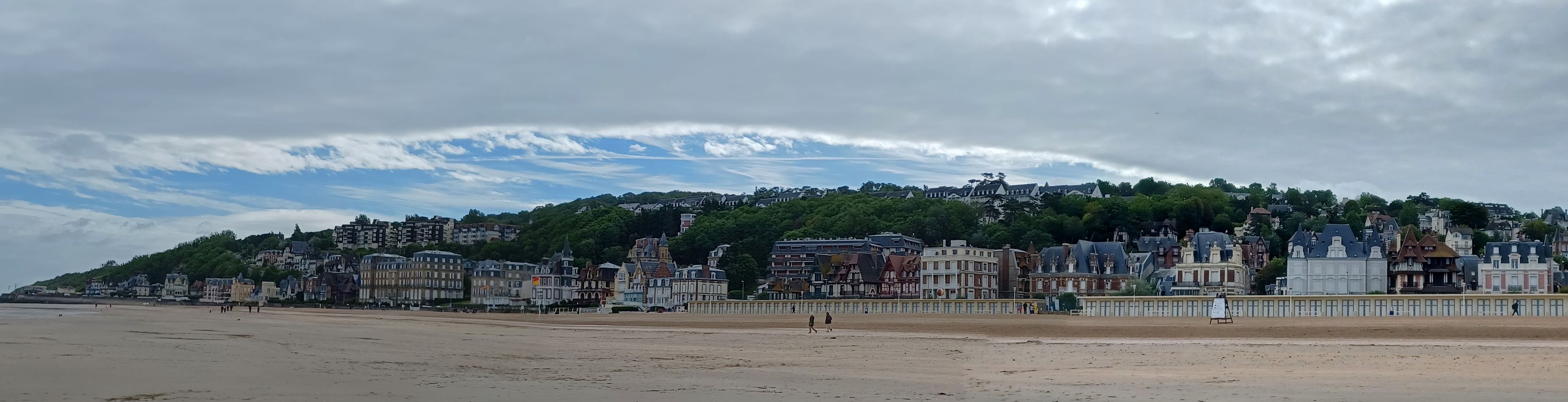 Une plage bordée d’une rangée de bâtiments historiques, avec une colline et des arbres en arrière-plan.
