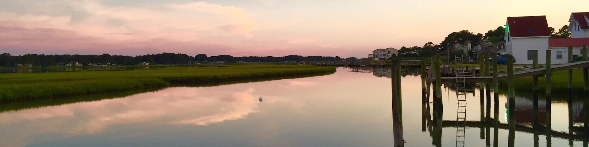 Une rivière paisible qui reflète le ciel, entourée de champs verdoyants et de maisons aux toits rouges.