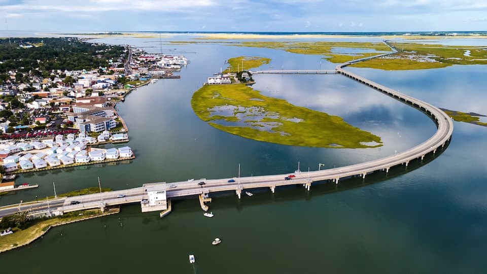 An aerial view of a coastal town with a curved bridge connecting to a peninsula.
