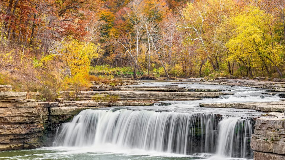 A waterfall cascading over rocky ledges surrounded by autumn-colored trees.