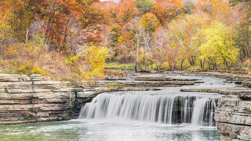 A waterfall cascading over rocky ledges surrounded by autumn-colored trees.