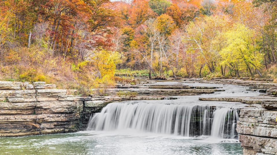 A waterfall cascading over rocky ledges surrounded by autumn-colored trees.