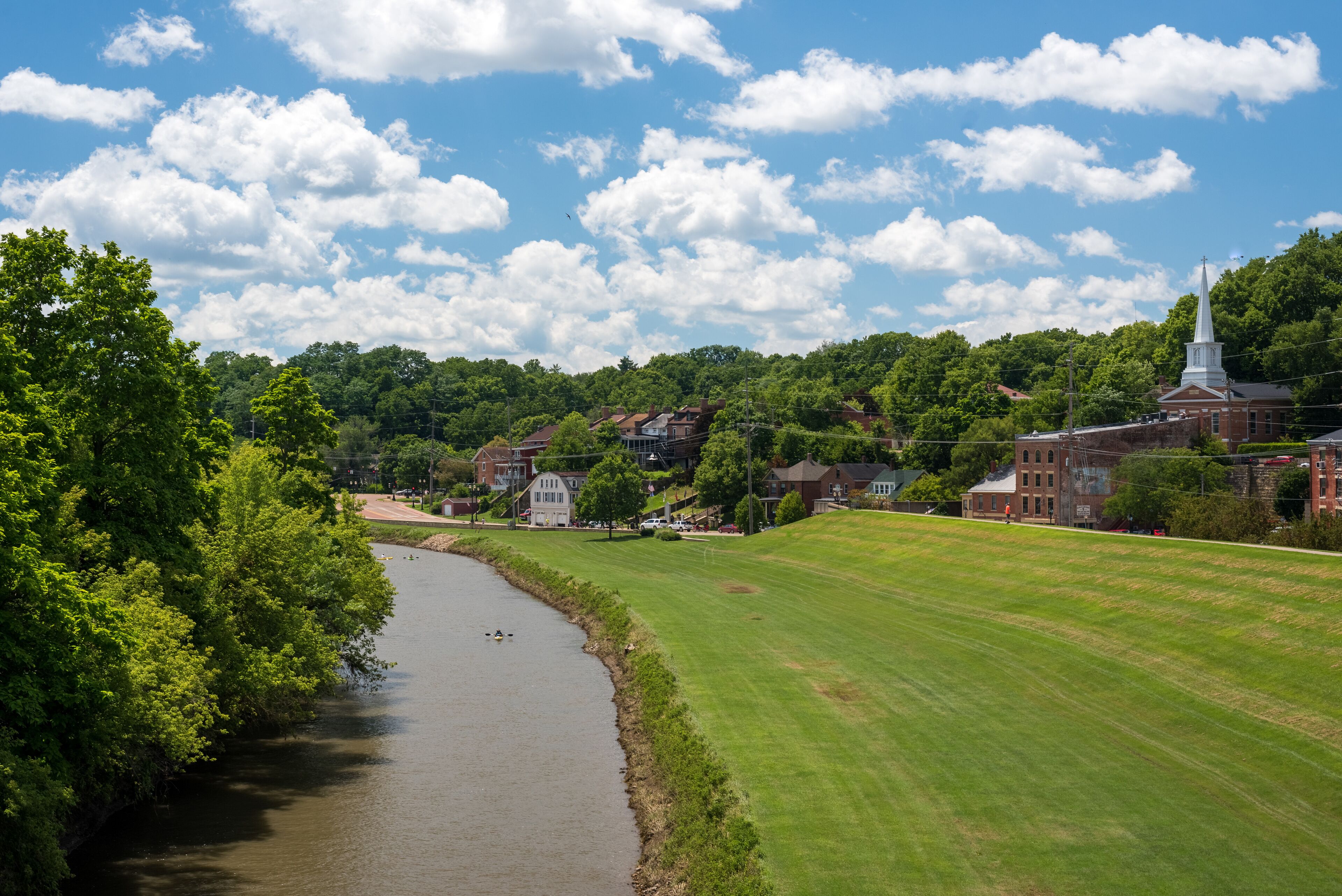 A river, green field, and a church with a steeple.