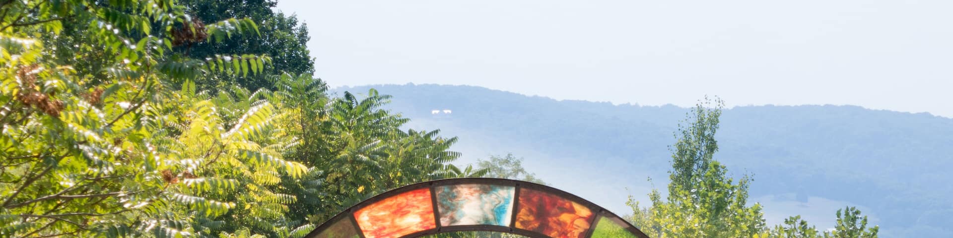 The Great Allegheny Passage rail trail showing colorful opalescent glass arch near Connellsville, PA, with mountain ridge in background