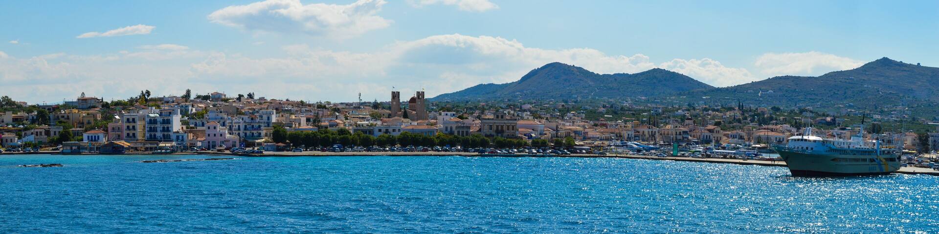 A coastal town with a harbor, boats, and a mountain range in the background.