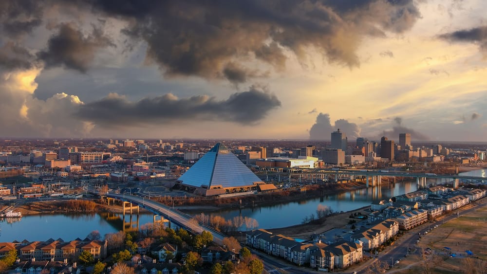Eine Stadtansicht mit einem markanten, pyramidenförmigen Gebäude, einem Fluss und einer Brücke.