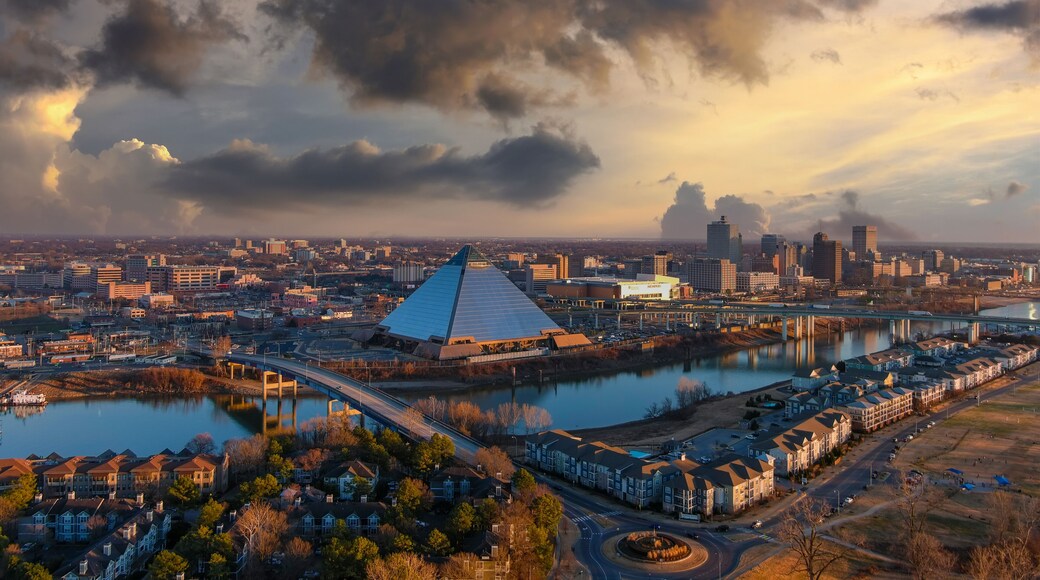a stunning aerial shot of the skyscrapers and office buildings in the cityscape along Wolf Creek Harbor with a glass pyramid with powerful clouds at sunset at Greenbelt Park on Mud Island in Memphis