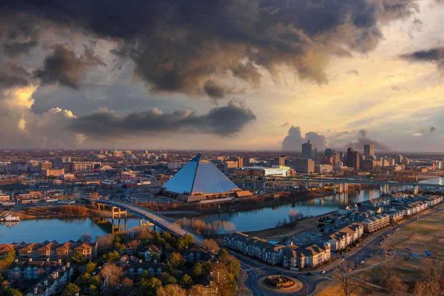 a stunning aerial shot of the skyscrapers and office buildings in the cityscape along Wolf Creek Harbor with a glass pyramid with powerful clouds at sunset at Greenbelt Park on Mud Island in Memphis