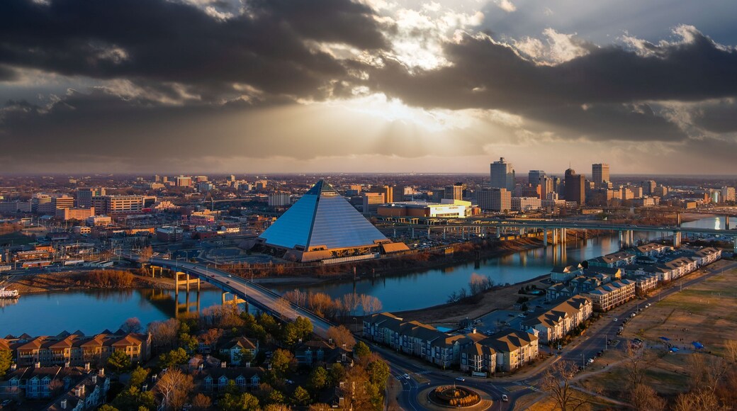 a stunning aerial shot of the the skyscrapers and office buildings in the cityscape along Wolf River Harbor with a glass pyramid and powerful clouds at sunset at Greenbelt Park on Mud Island