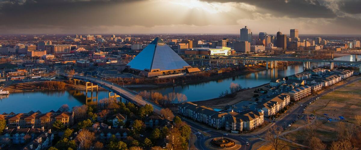 Eine Stadtansicht mit einem markanten pyramidenförmigen Gebäude, einem Fluss und einer Brücke.
