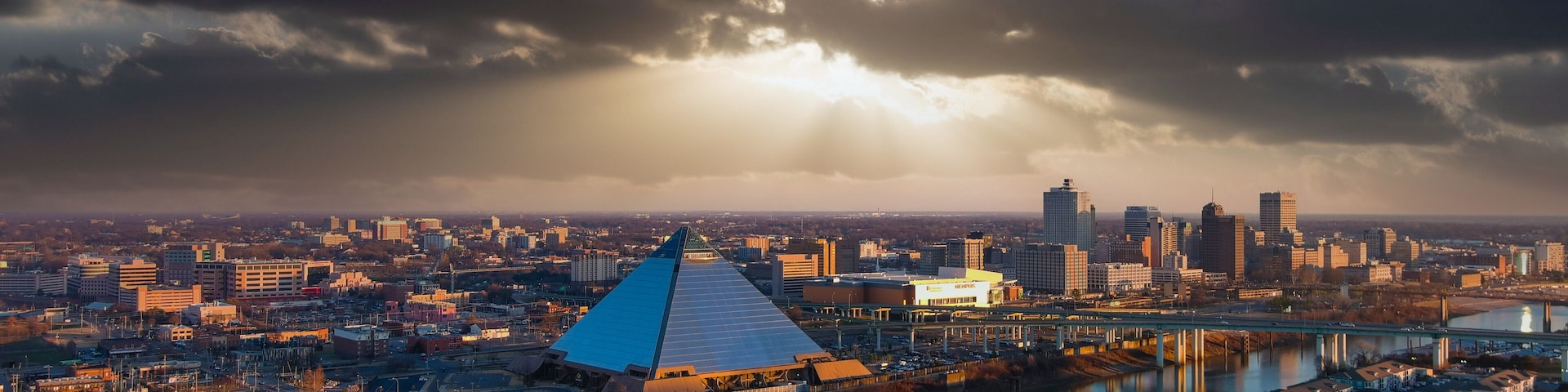 Eine Stadtansicht mit einem markanten pyramidenförmigen Gebäude, einem Fluss und einer Brücke.