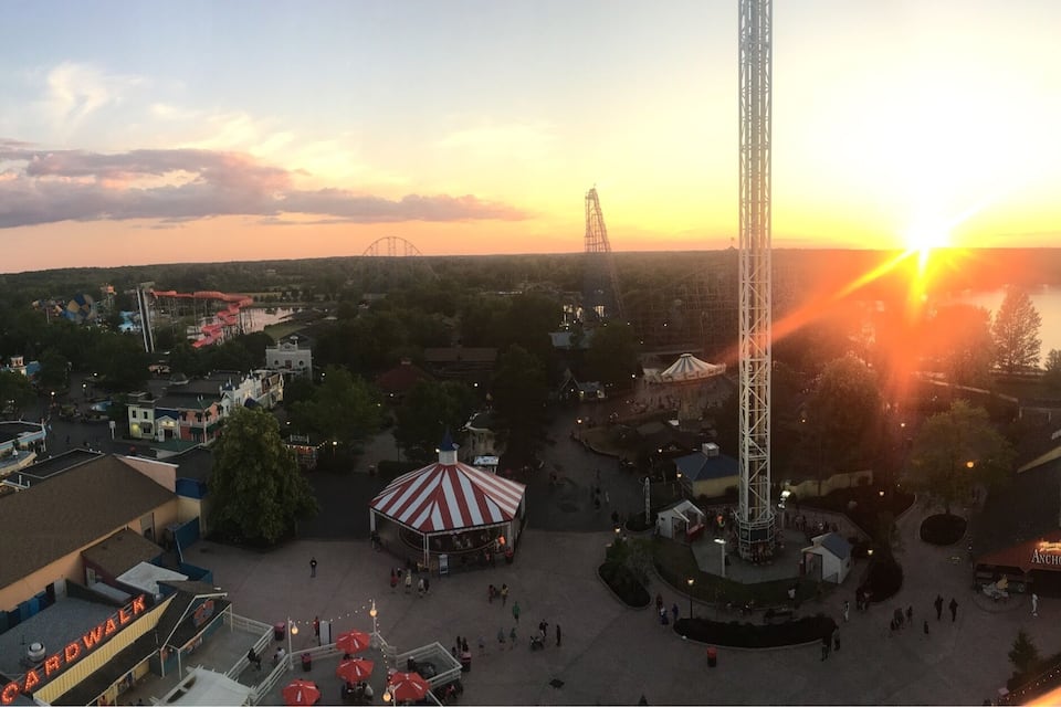 A theme park at sunset with a Ferris wheel, a tall tower, and a carousel.