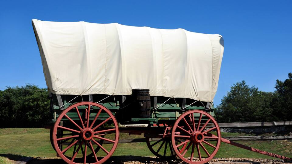 A covered wagon with red wheels parked on a paved area.