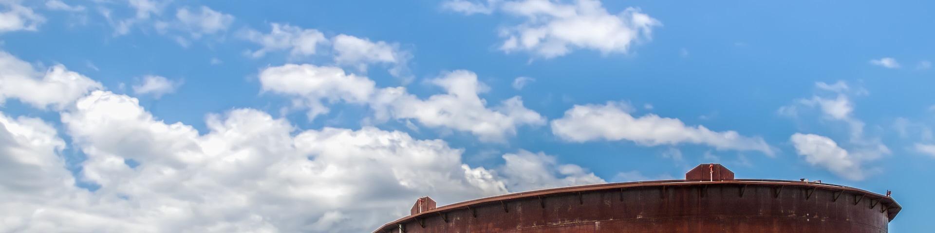 Large cylindrical storage tanks under a partly cloudy sky.