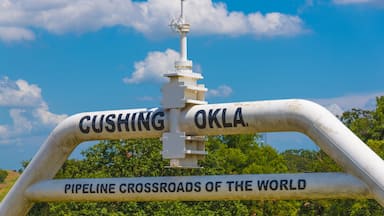 A large metal archway with the inscription "CUSHING OKLA. PIPELINE CROSSROADS OF THE WORLD" against a backdrop of a clear blue sky and green trees.