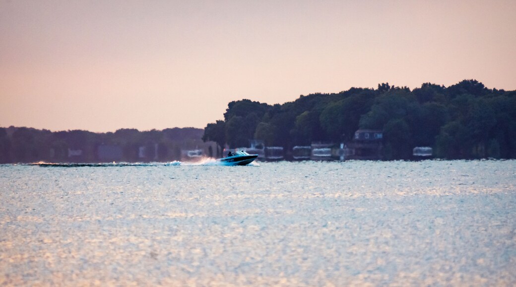 Motorboat cruising across a calm lake during a hazy summer sunrise in Waukesha County, Wisconsin. Early morning July light on the water.