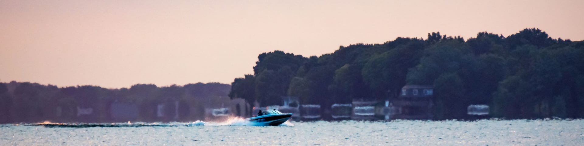 Motorboat cruising across a calm lake during a hazy summer sunrise in Waukesha County, Wisconsin. Early morning July light on the water.
