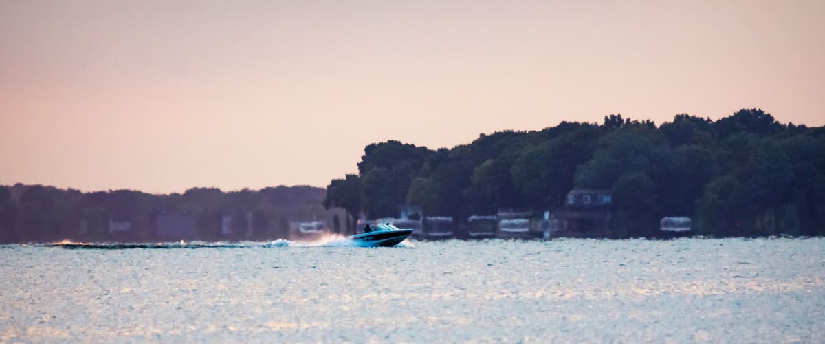 A boat on a calm lake with a forested shoreline in the background.