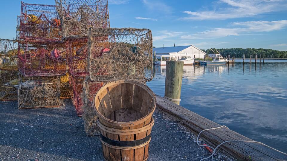A dock with lobster traps and a wooden bucket by the water.