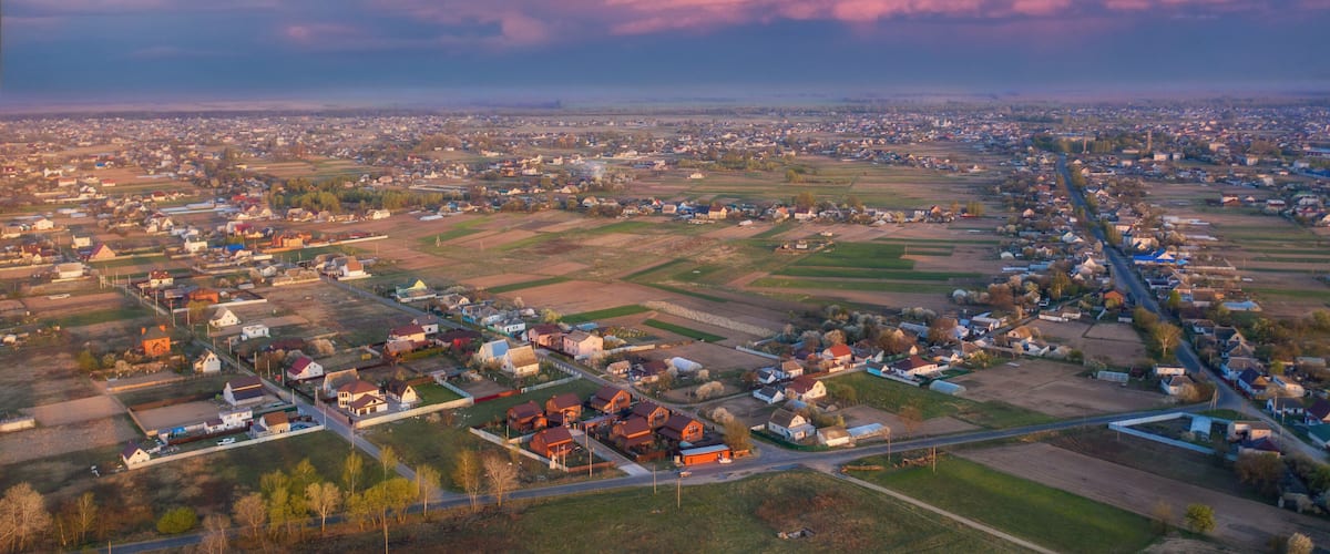 An aerial view of a town with a river running through it, surrounded by fields and houses.