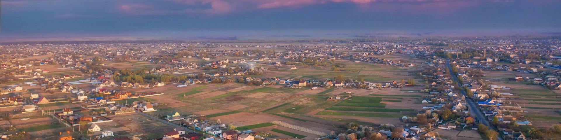 An aerial view of a town with a river running through it, surrounded by fields and houses.