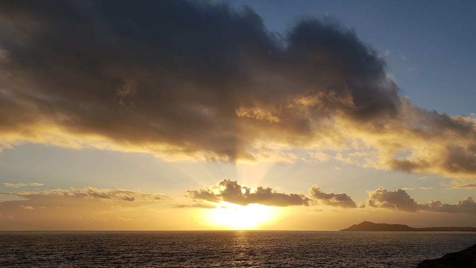 A sunset over the ocean with clouds and a silhouette of a mountain.