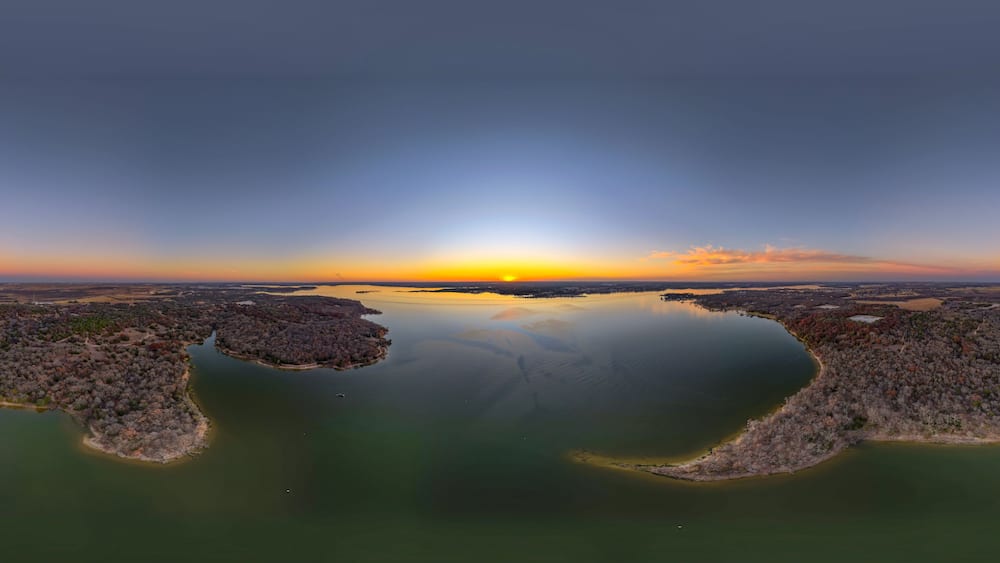 A sunset over a calm lake with two islands surrounded by trees.