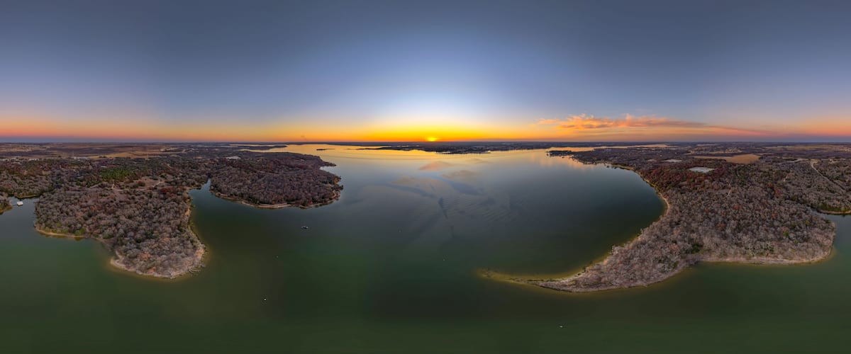 A sunset over a calm lake with two islands surrounded by trees.