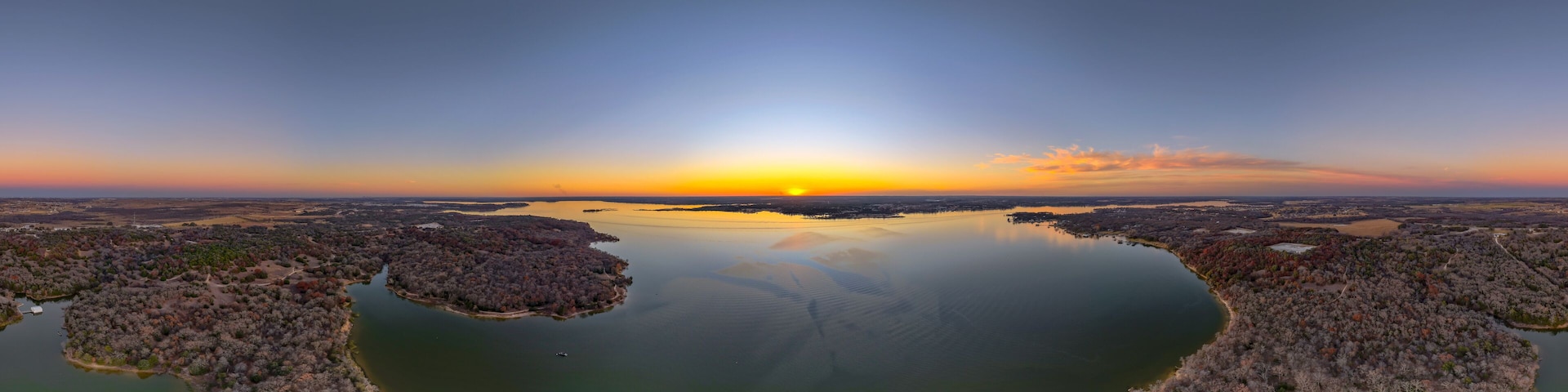 A sunset over a calm lake with two islands surrounded by trees.