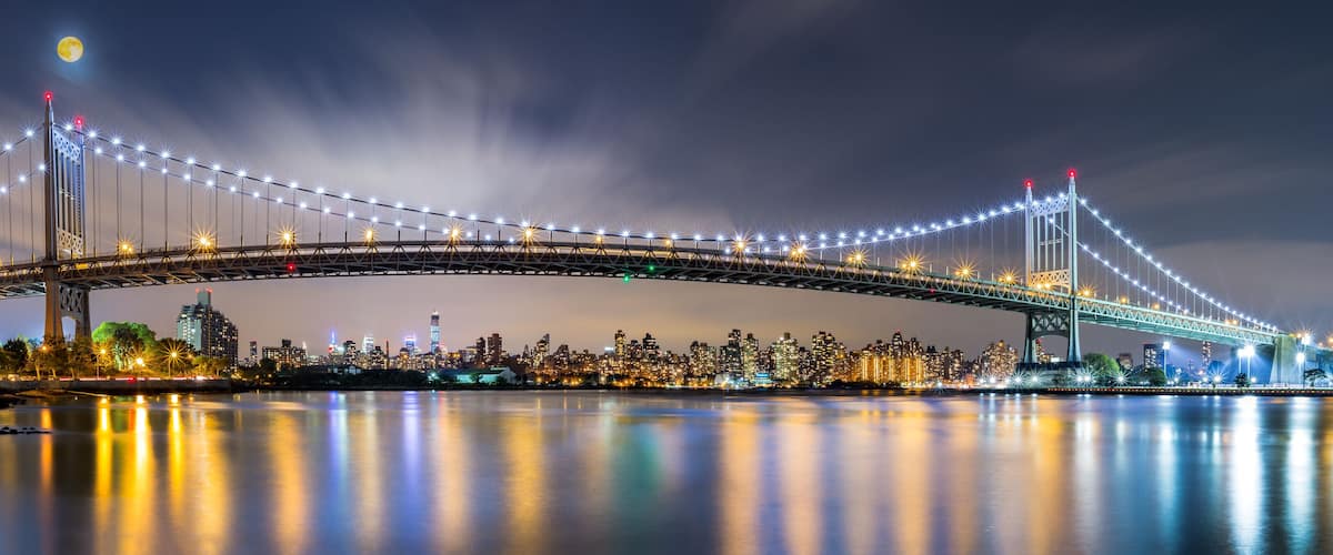 A brightly lit bridge with lights reflecting on the water at night.