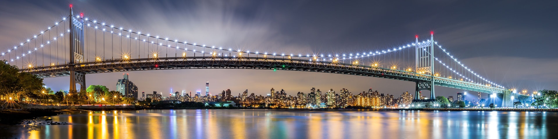 A brightly lit bridge with lights reflecting on the water at night.