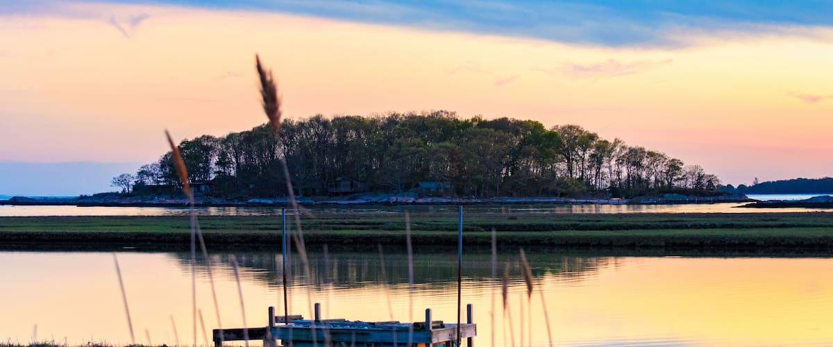 Tidal marsh at sunset, Niantic Connecticut with view of dock and Watts Island at sunset, blue hour. Golden hour sky with trees and island in silhouette.
