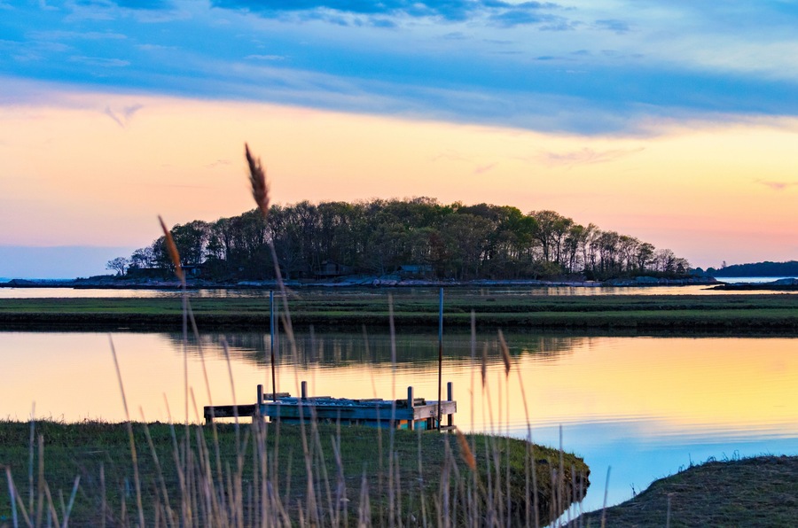 Tidal marsh at sunset, Niantic Connecticut with view of dock and Watts Island at sunset, blue hour. Golden hour sky with trees and island in silhouette.
