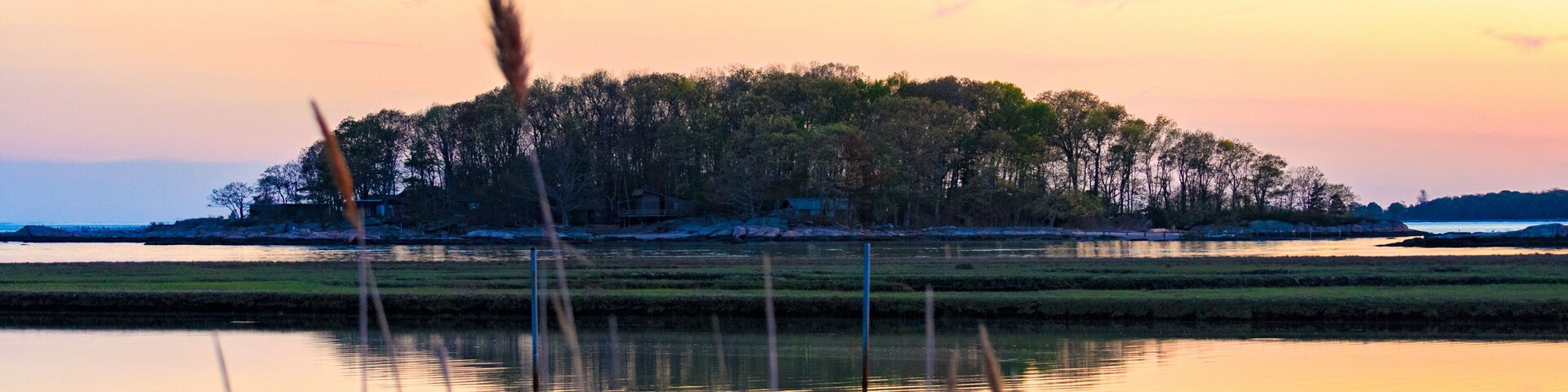 Tidal marsh at sunset, Niantic Connecticut with view of dock and Watts Island at sunset, blue hour. Golden hour sky with trees and island in silhouette.