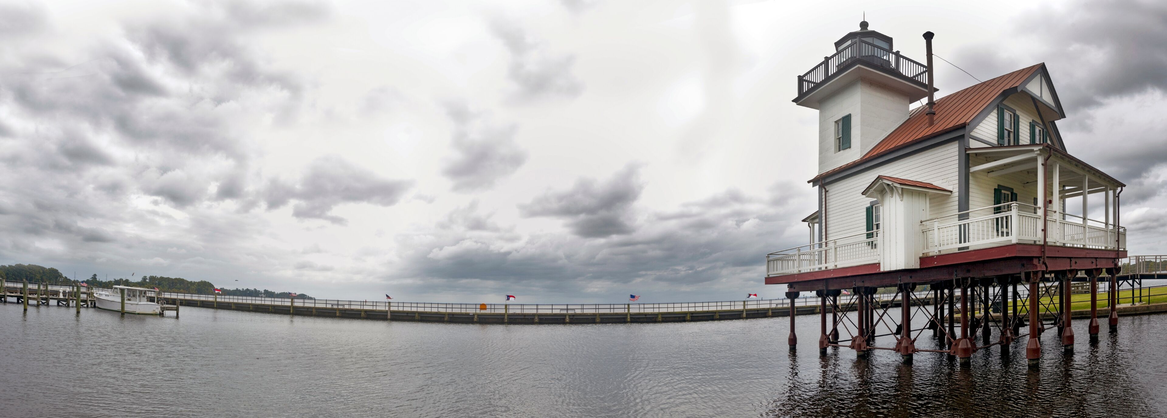 A lighthouse on stilts over water with a cloudy sky.
