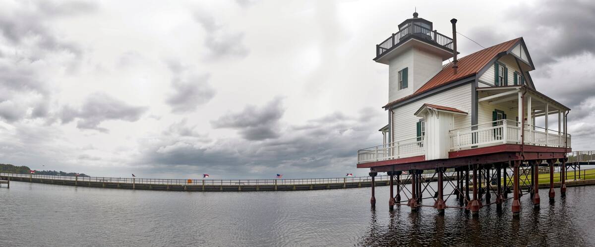 A lighthouse on stilts over water with a cloudy sky.