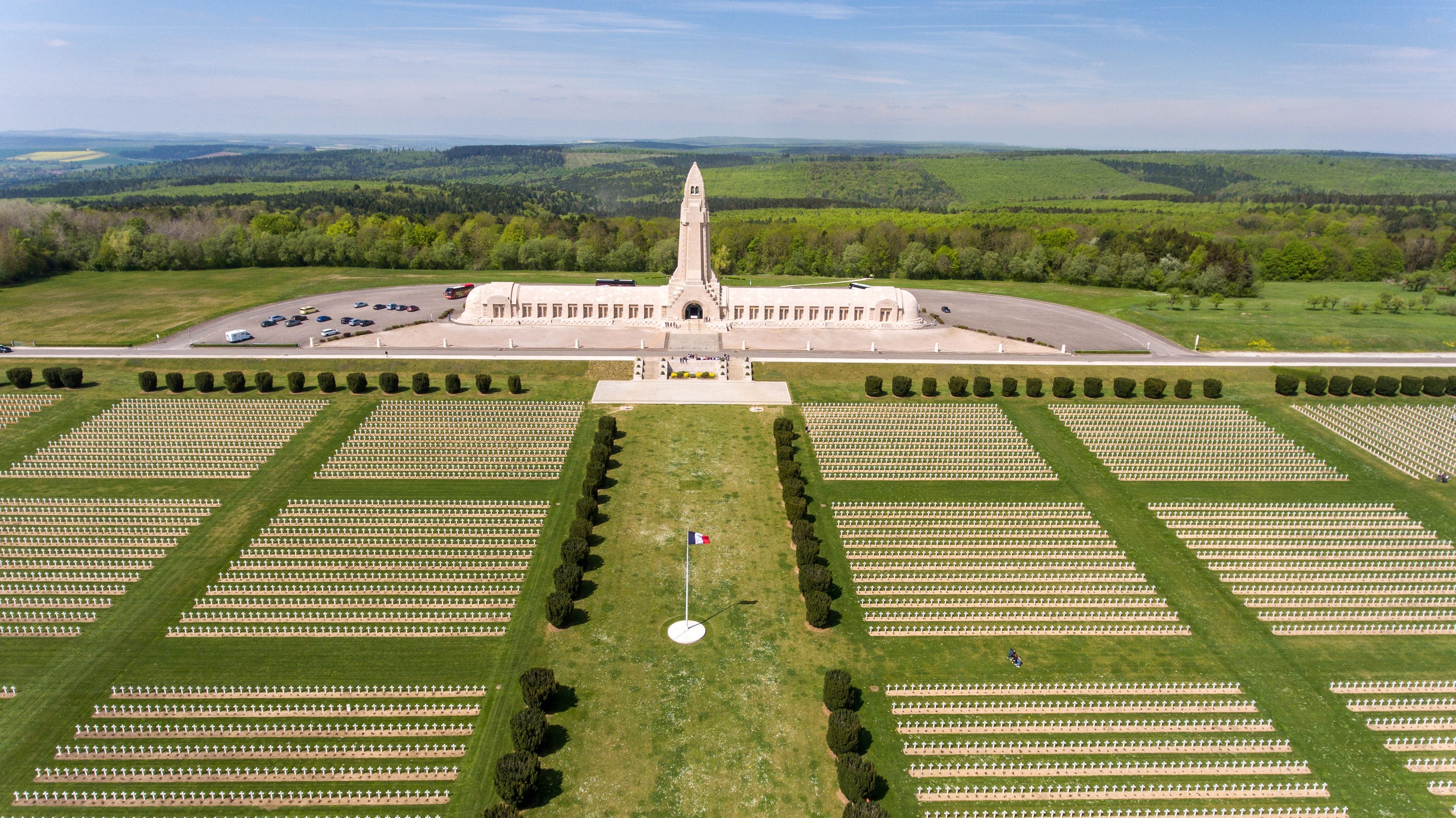 A large cemetery with rows of graves, a central monument, and a surrounding landscape.