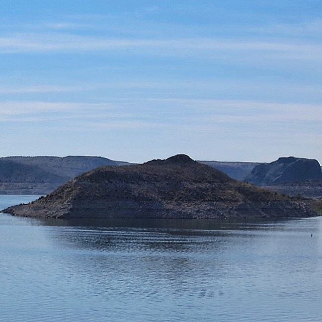 Un lago tranquilo con una pequeña isla en el centro y colinas distantes.