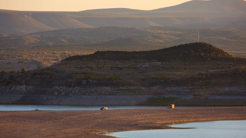 A desert landscape with a hill, a small body of water, and a vehicle.