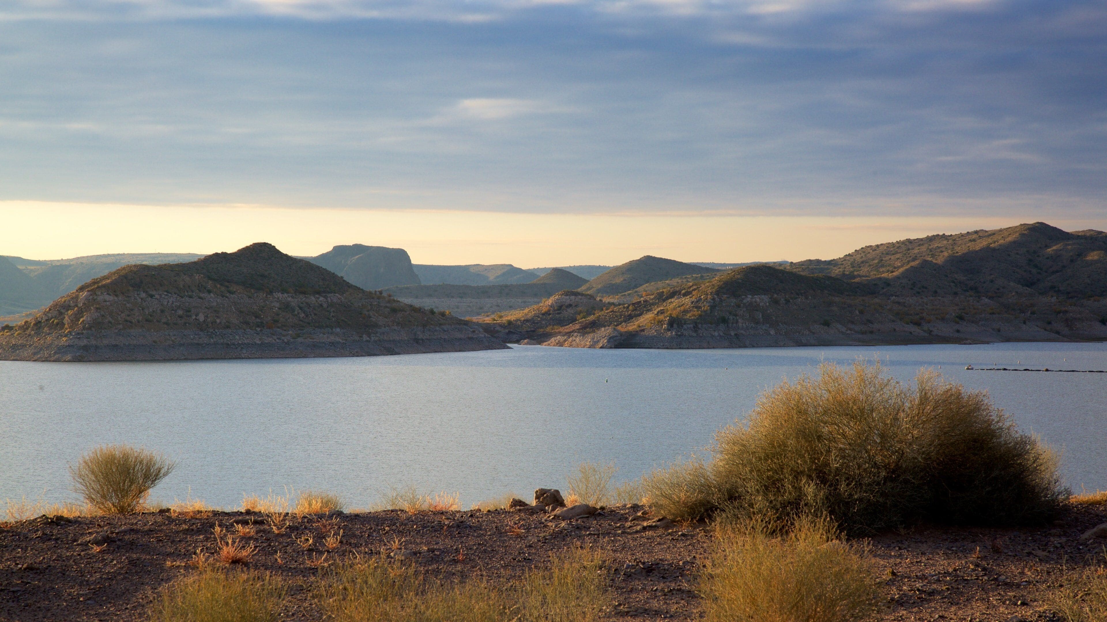 A lake surrounded by hills and sparse vegetation.