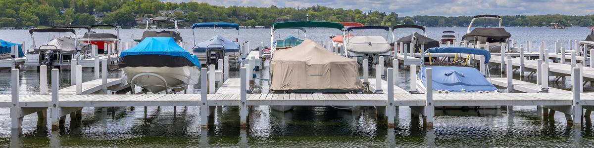 Covered boats and pontoon boats at a pier on a lake with dramatic clouds.
