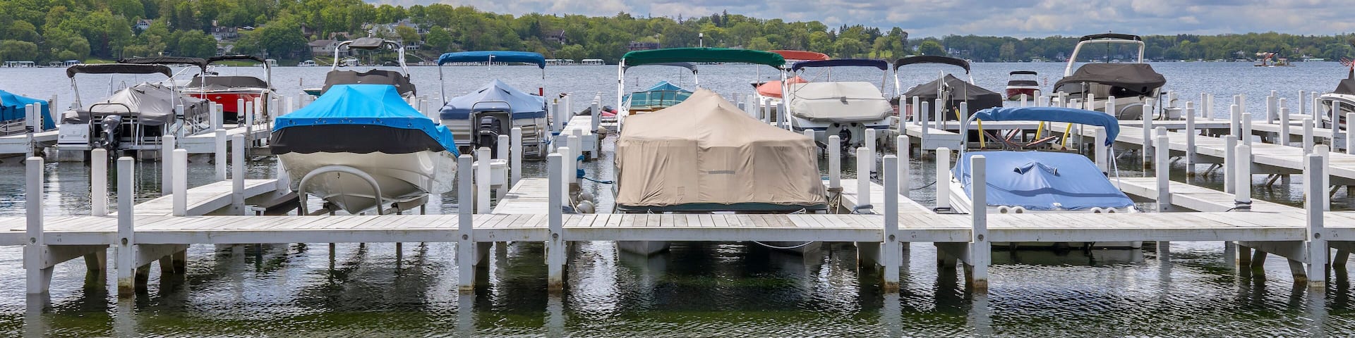 Covered boats and pontoon boats at a pier on a lake with dramatic clouds.