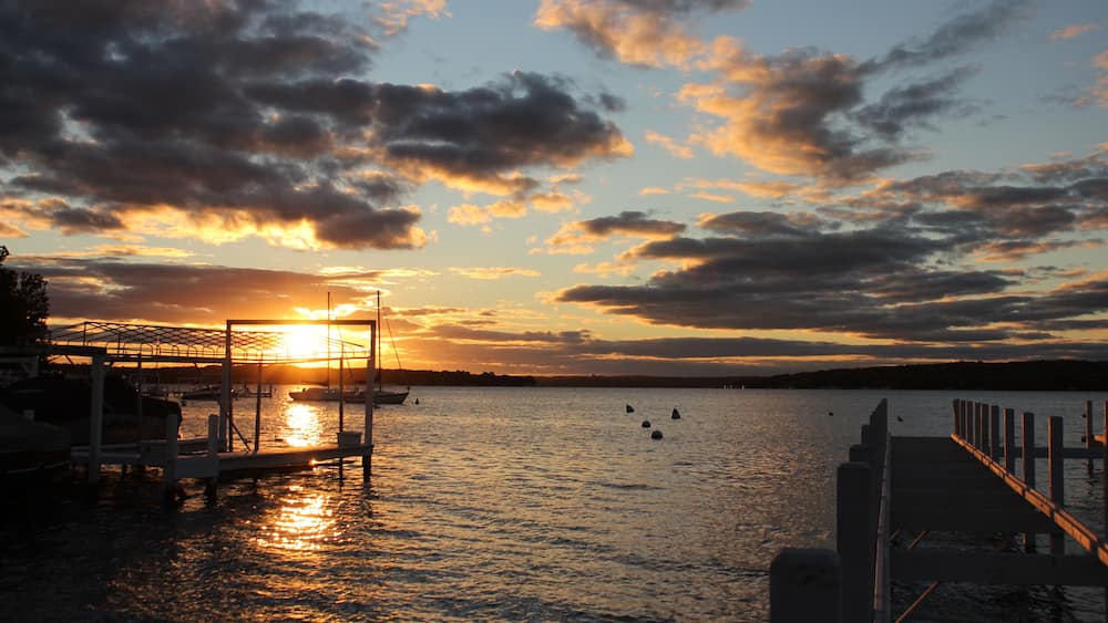 A sunset over a calm body of water with boats docked at a pier.