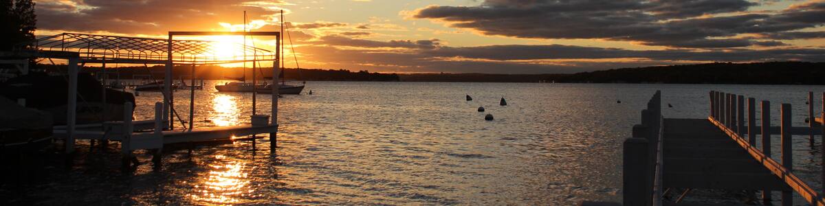 Un coucher de soleil sur une étendue d’eau calme, avec des bateaux amarrés à un quai.