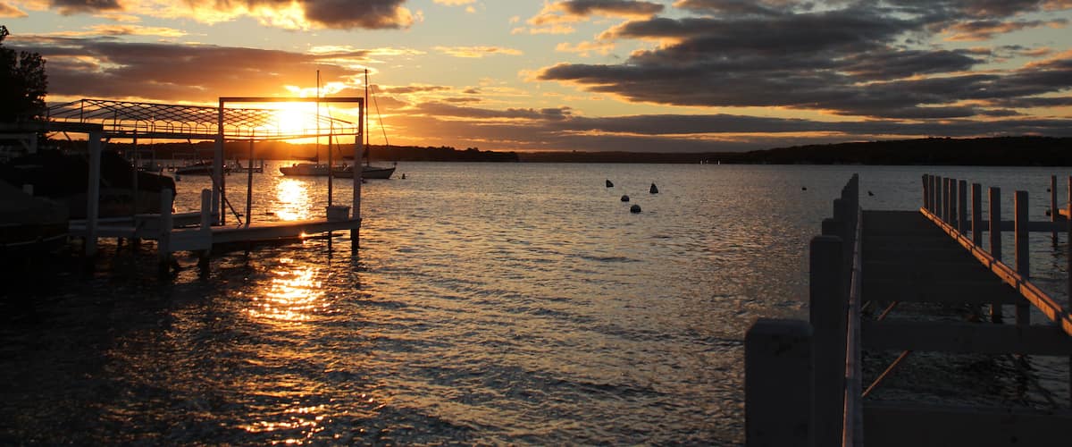 Ein Sonnenuntergang über ruhigem Wasser, mit Booten, die an einem Steg vertäut sind.