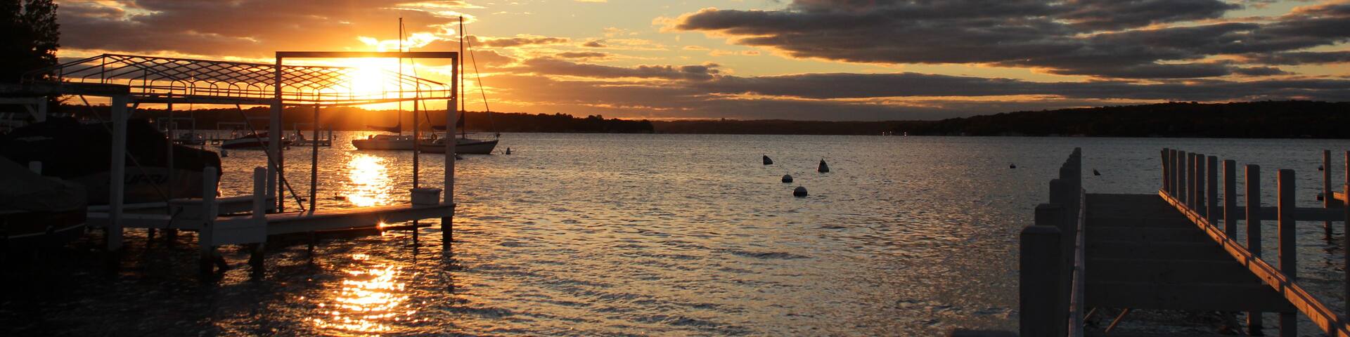 A sunset over a calm body of water with boats docked at a pier.