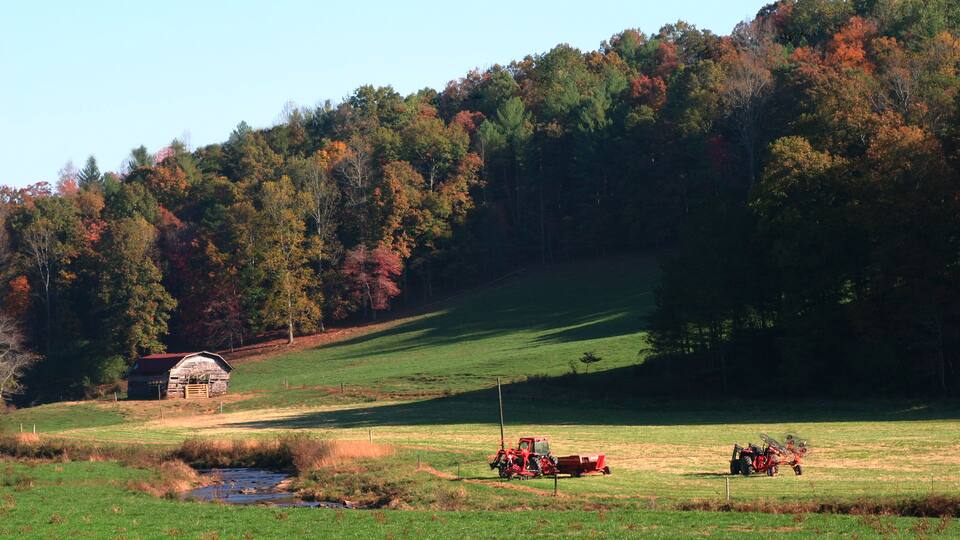 A rural landscape with a barn, a tractor, and a stream.